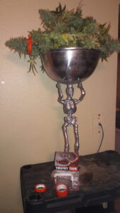 A metal skeleton figurine holding up a metallic bowl.