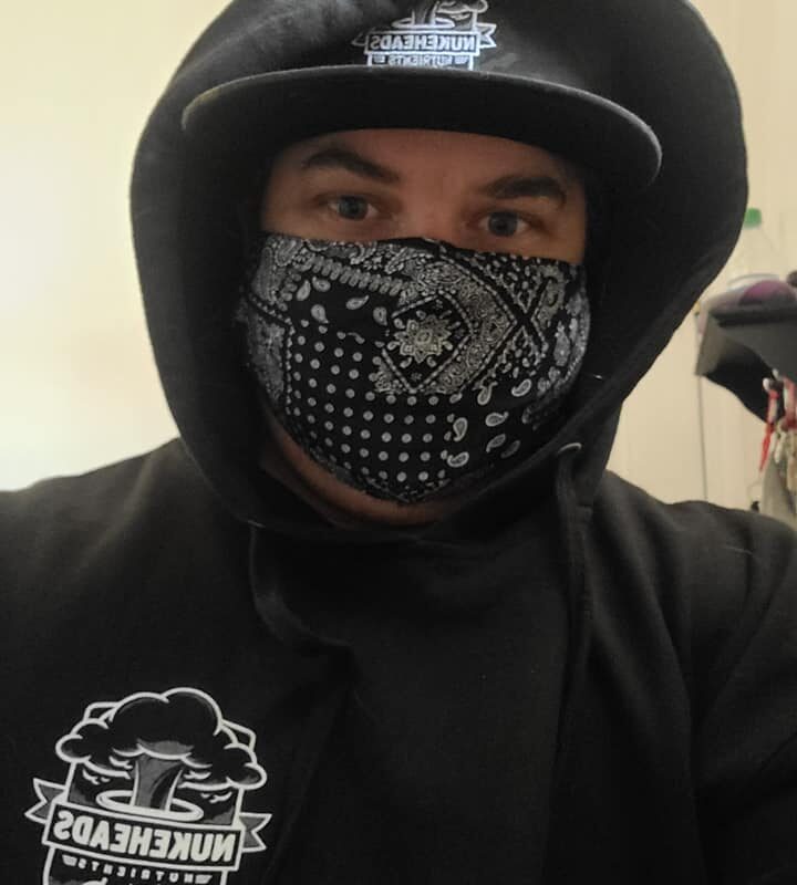 Person wearing a black hoodie, helmet, and patterned face mask.