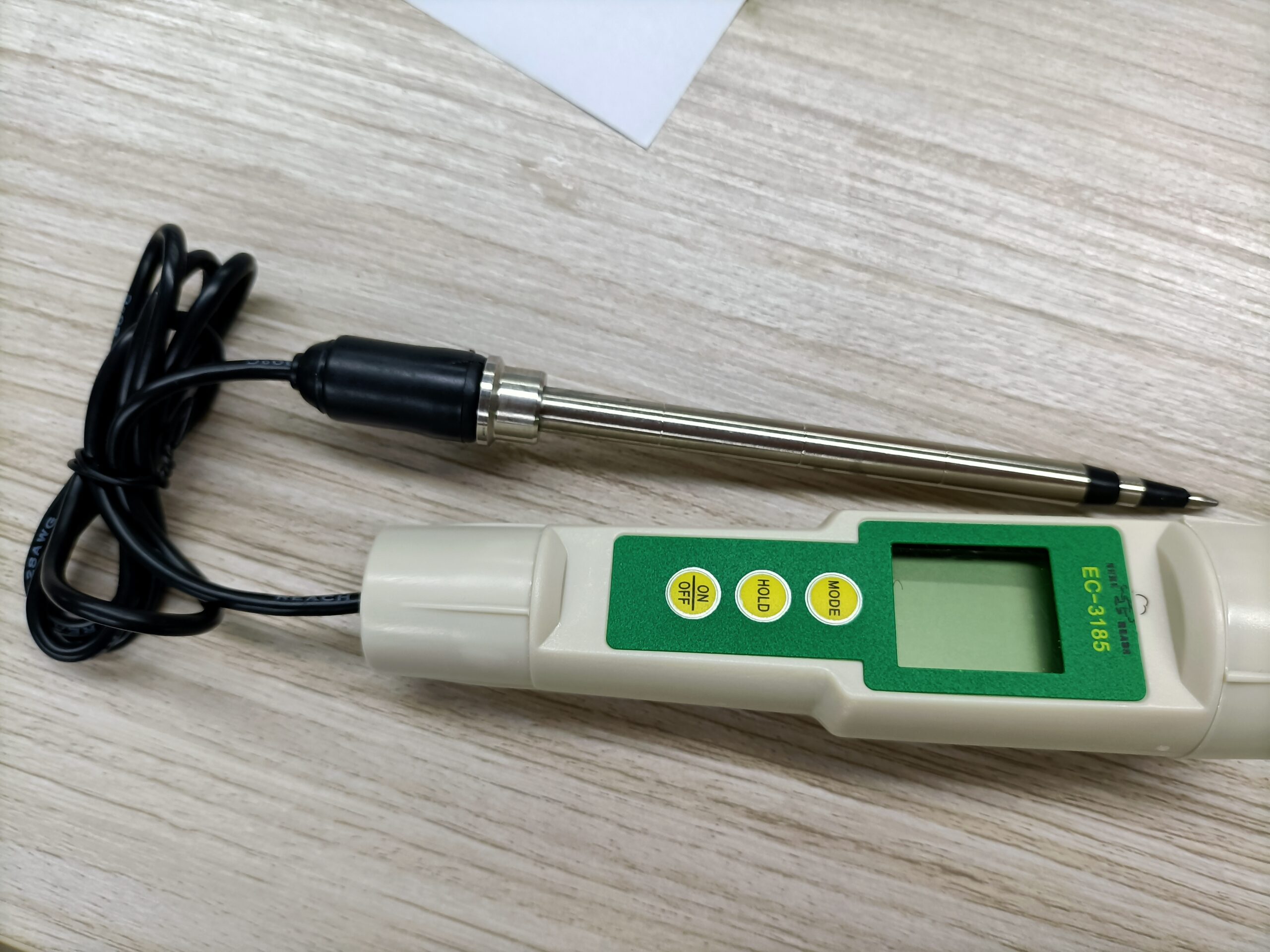 Digital conductivity meter on wooden surface.